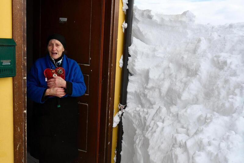 A woman stands by a wall of snow next to the door of her home in the village of Campotosto, in the mountainous region of central Italy on January 19, 2017. The area has been hit by a series of quakes since August, including one on Thursday that triggered an avalanche, burying an alpine hotel and about 30 occupants. Claudio Lattanzio / ANSA via AP