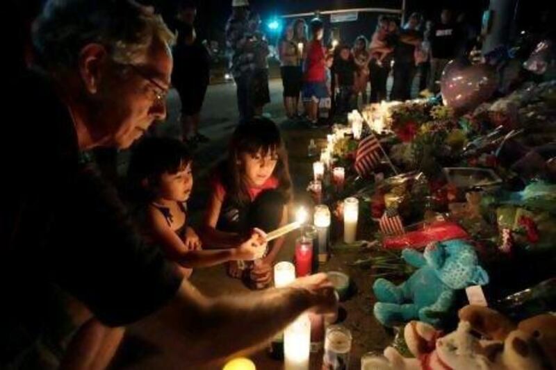 Ted Engelmann, left, helps Yamilet Ortega, 3, and Kimberly Hernandez, 7, light candles at a memorial near the cinema in Colorado where a gunman killed at least 12 people in one of the deadliest mass shootings in recent US history.