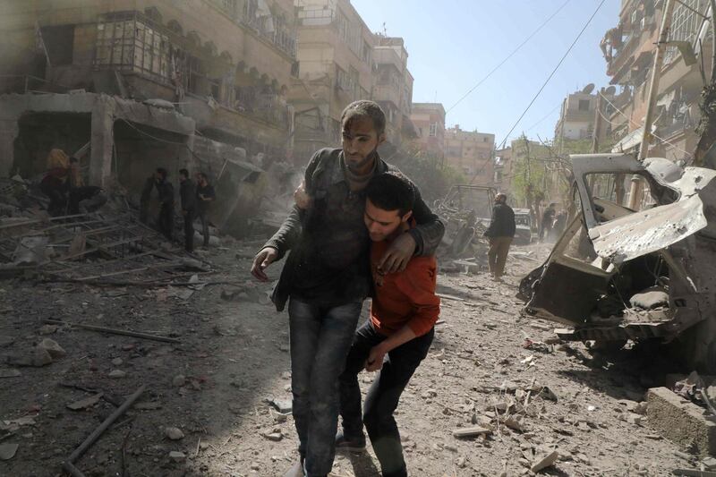 TOPSHOT - A Syrian man helps evacuate an injured victim following Syrian government air strikes on the Eastern Ghouta rebel-held enclave of Douma, on the outskirts of the capital Damascus on March 20, 2018.
Syrian regime and allied forces battled to suppress the last pockets of resistance in and around Damascus while the beleaguered Kurds in the north braced for further Turkish advances. Assad has in recent months brought swathes of territory back under his control thanks to heavy Russian involvement, as well as support from other forces such as the Iran-backed Lebanese Hezbollah militia. Eastern Ghouta's main town of Douma remains under rebel control but even as a trickle of emergency medical evacuations was scheduled to continue, the regime continued to pound the enclave. / AFP PHOTO / HAMZA AL-AJWEH