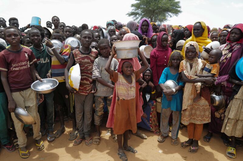 Sudanese children who fled the conflict in Geneina in Sudan's Darfur region, line up to receive rice portions from Red Cross volunteers in Ourang on the outskirts of Adre, Chad.