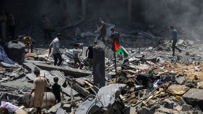 A Palestinian flag flies among the rubble as people inspect the damage following an Israeli air strike on Al Bureij refugee camp. EPA