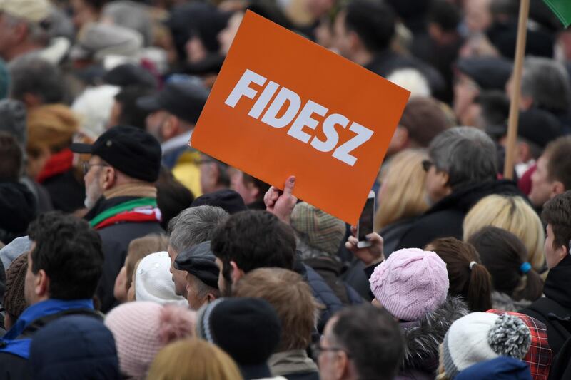 A supporter holds a sign of the governing FIDESZ party in front of the Hungarian Parliament as the Hungarian Prime Minister delivers a speech in Budapest on March 15, 2018, during the official commemoration of the 170th anniversary of the 1848-1849 Hungarian revolution. 
Tens of thousands of Hungarians took to the streets Thursday in separate national day demonstrations to both voice support for, and protest against, Prime Minister Viktor Orban, as an election April 8 nears. / AFP PHOTO / Attila KISBENEDEK