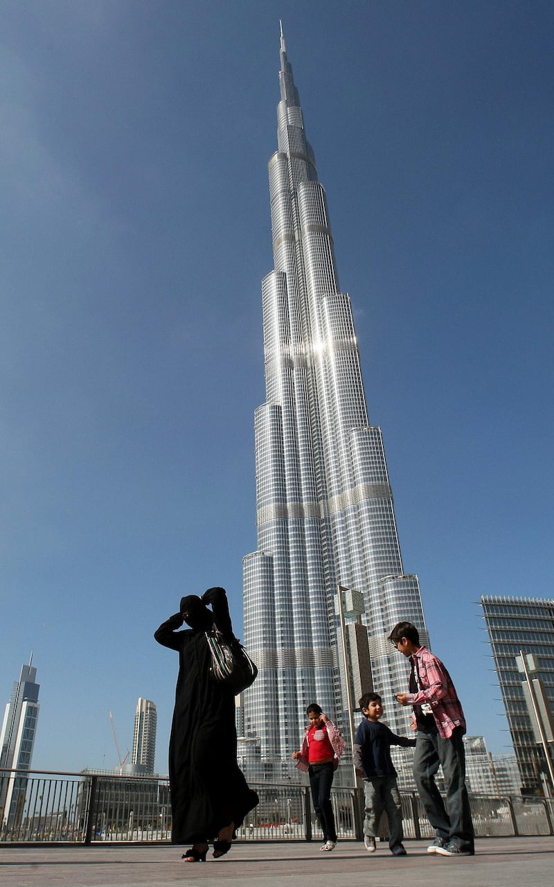 (FILES) A picture taken on January 3, 2010 shows an Emirati woman and her children walking past Burj Khalifa, the world's tallest tower, in Dubai. Dubai's debt-laden group, Dubai World, said on May 20, 2010 it has reached an agreement "in principle" with most of its bank lenders to restructure some 23.5 billion dollars in debt. AFP PHOTO/KARIM SAHIB (Photo by KARIM SAHIB / FILES / AFP)