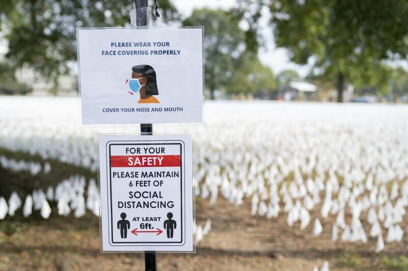 Signs encouraging protective masks and social distancing in front of white flags representing the number of Americans who have died of Covid-19 at the DC Armory Parade Grounds in Washington, DC, US. Bloomberg
