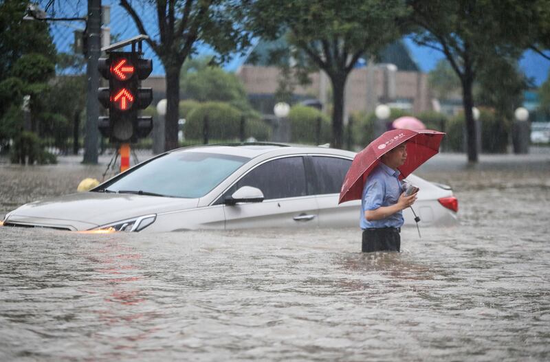 A man wades past a submerged car following heavy rains in Zhengzhou in central China's Henan province.