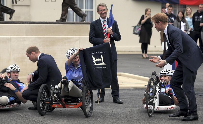 TIDWORTH, ENGLAND - MAY 20:  Prince Harry (R) receives a Help for Heroes hooded top from Corporal Claire Edwards (C) who is taking place in the 2013 Hero Ride, as he officially open the charity's Tedworth House recovery centre on May 20, 2013 in Tidworth, England. During their visit the two Royal Princes met with wounded veterans, serving personnel, and their families. Tedworth House in Wiltshire is one of four new units in England which will offer respite care and rehabilitation to injured and sick service personnel, veterans and their families.  (Photo by Matt Cardy/Getty Images)