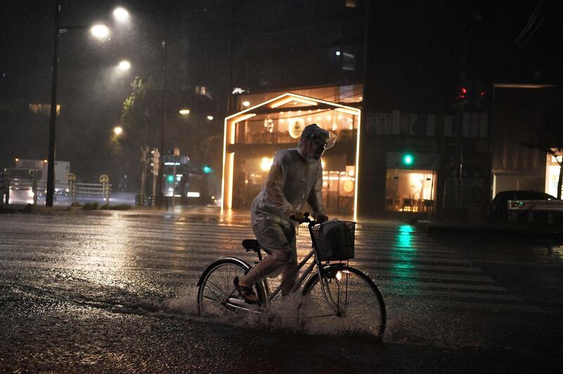 A man rides his bicycle under the rain as a typhoon hits Tokyo by night on September 9, 2019. A strong typhoon that could bring record winds and rain was poised to make a direct hit on Tokyo later September 8, as authorities issued evacuation warnings amid a risk of high waves, landslides and flooding. / AFP / Charly TRIBALLEAU
