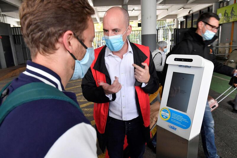 An agent helps a man taking his body temperature in front of a "health terminal" installed on a platform at the Matabiau train station in Toulouse, on October 6, 2020.  The SNCF is offering volunteer passengers the opportunity to try out a device that allows them to check their body temperature before boarding the TGV in Ouigo. The "health terminals" are equipped with a thermal camera that measures body temperature without contact. / AFP / GEORGES GOBET
