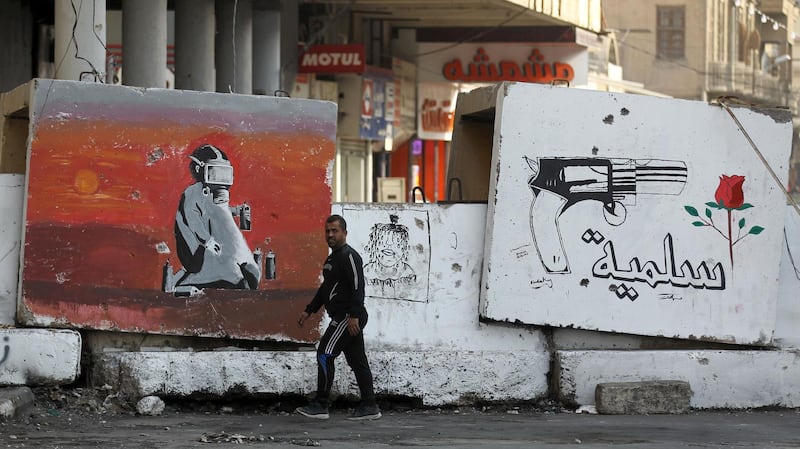 TOPSHOT - This picture taken on December 25, 2019 shows a view of a concrete barrier part of a barricade along Rasheed street in the Iraqi capital Baghdad, with a graffiti mural depicting a gun before a flower and text in Arabic reading "peaceful".  / AFP / AHMAD AL-RUBAYE
