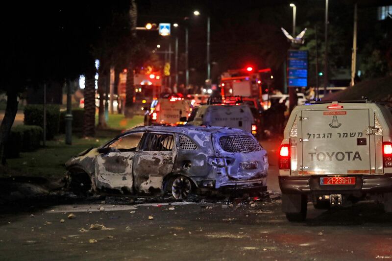 Israeli border police vehicles drive past an extinguished burnt vehicle in Lod near Tel Aviv, after rockets were launched towards Israel from the Gaza Strip controlled by the Palestinian Hamas movement.  AFP