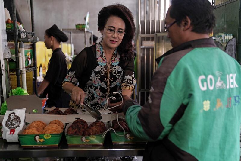 Nanik Soelistiowati, the owner of Pisang Goreng Bu Nanik, left, prepares an order for a Gojek driver at her shop in Jakarta, Indonesia, on Monday, July 15, 2019. Globally, the online food order industry has grown into a hyper-competitive field, which has led to consolidation as companies claw for a bigger slice of more than $300 billion in restaurant deliveries. Photographer: Dimas Ardian/Bloomberg