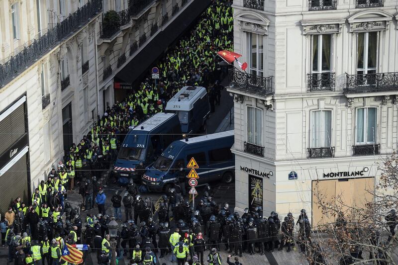 Protestors wearing "yellow vests" (gilets jaunes) walk past police vans near the Champs Elysees avenue in Paris.  AFP