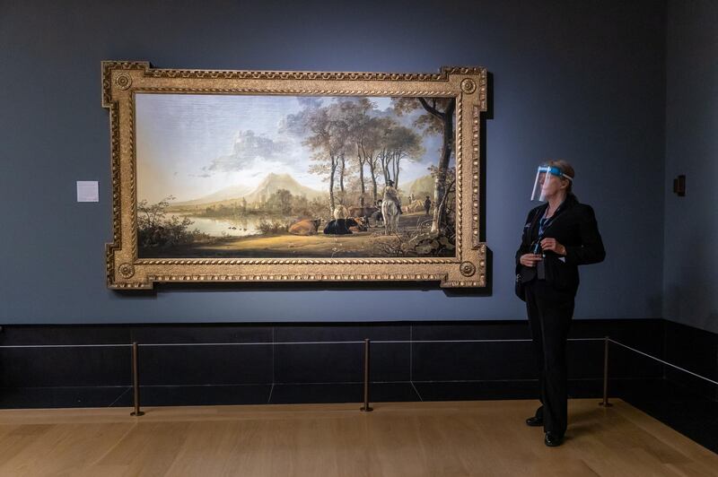 A member of staff wearing a face shield stands next to 'River Landscape with Horseman and Peasants' by Aelbert Cuyp at the National Gallery in London. EPA