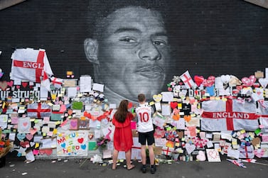 Mackenzie Robertson aged 15 and his mother Sally Coles-Roberton place a message of support on a mural of Manchester United striker and England player Marcus Rashford, on the wall of the Coffee House Cafe on Copson Street, in Withington, Manchester, England, Tuesday July 13, 2021.  The mural was defaced with graffiti in the wake of England losing the Euro 2020 soccer championship final match to Italy.  (AP Photo / Jon Super)