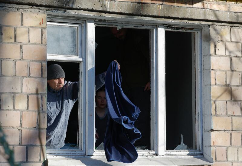A man shakes out a blanket from a window broken during the explosions. EPA