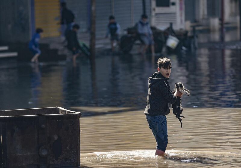 A young Palestinian boy holding a cat walks through floodwaters following heavy rains in Jabalia refugee camp in northern Gaza strip. AFP