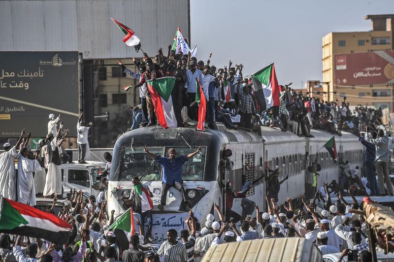 CORRECTION / Sudanese protesters from the city of Atbara, sitting atop a train, cheer upon arriving at the Bahari station in Khartoum on April 23, 2019. The passengers, who had travelled from the town of Atbara where the first protest against ousted president Omar al-Bashir erupted on December 19, chanted "freedom, peace, justice". Many protesters perched on the roof of the train, waving Sudanese flags as it chugged through north Khartoum's Bahari railway station before winding its way to the protest site, an AFP photographer said. / AFP / OZAN KOSE
