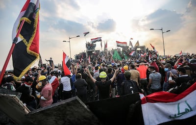 (FILES) In this file photo taken on October 29, 2019, Iraqi protesters wave national flags as they stand atop concrete barriers across the capital Baghdad's al-Jumhuriya bridge which connects between Tahrir Square and the high-security Green Zone, hosting government offices and foreign embassies, during the ongoing anti-government protests. In October 2019, unprecedented demonstrations across Iraq demanded the downfall of the ruling class. But after a year, a new government and nearly 600 protesters killed, virtually nothing has changed. / AFP / AHMAD AL-RUBAYE
