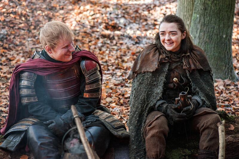 This image released by HBO shows Ed Sheeran, left, and Maisie Williams in a scene from "Game of Thrones." Sheeran appeared as a Lannister soldier leading a group in song in the season premiere of the hit HBO fantasy drama, which debuted on the premium cable channel Sunday night. (Helen Sloan/HBO via AP)