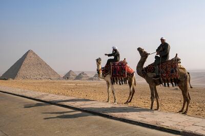 Camel trainers ride camels awaiting tourists by the Pyramid of Menkaure (Menkheres) at the Giza Pyramids Necropolis on the western outskirts of the Egyptian capital's twin city of Giza on January 7, 2021. (Photo by Amir MAKAR / AFP)