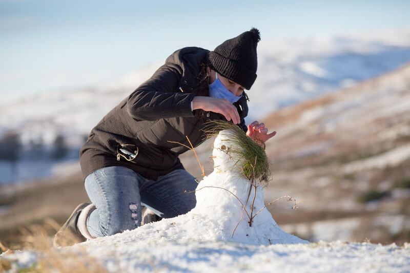 A woman tries to make a snowman in the snow at Campsie Fells, Glasgow. EPA