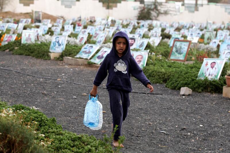 A Yemeni child holding empty bottles walks past portraits on the graves of Yemenis at a cemetery in Sanaa.  EPA