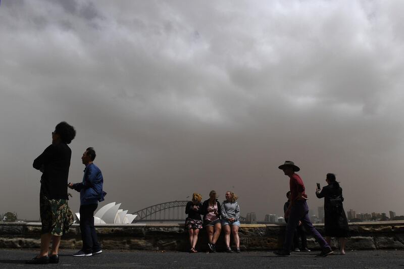 Tourists take photographs against the backdrop of the Sydney Harbour Bridge and the Sydney Opera House as a dust storm descends on Sydney, Australia. EPA