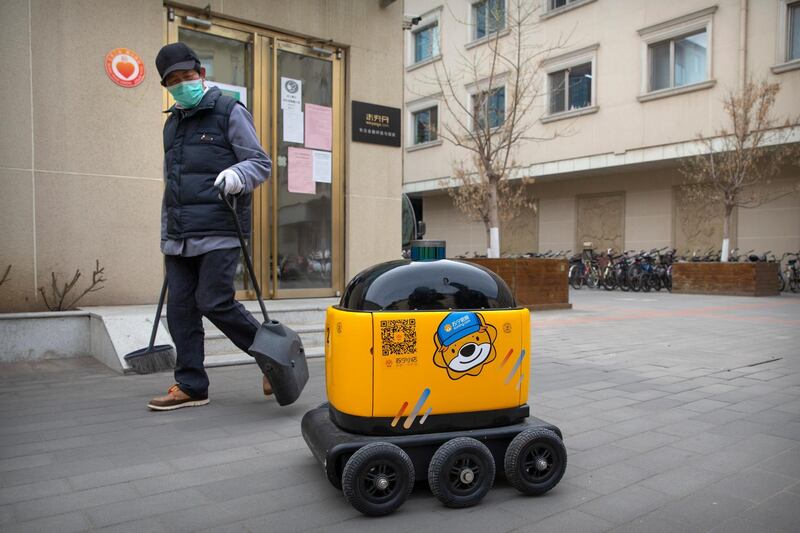 In this March 18, 2020, photo, a maintenance worker looks at a robot outside the offices of ZhenRobotics in Beijing. While other industries struggle, one robot maker says China's virus outbreak is boosting demand for his knee-high, bright yellow robots to deliver groceries and patrol malls for shoppers who fail to wear masks. (AP Photo/Mark Schiefelbein)