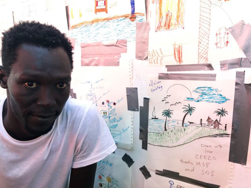 A rescued migrant called Ezzo poses next to his drawing depicting his village at the bottom of the Nuna Mounts in southern Sudan. AFP