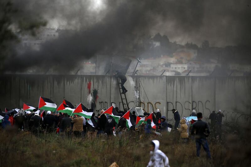 TOPSHOT - A Palestinian protester escalates Israel's controversial security wall as others waving national flags burn tyres during a demonstration against a US-brokered peace proposal, in the occupied West Bank village of Bilin near Ramallah on February 7, 2020.  The Jewish settlement of Modiin Illit can be seen in the background. Israel deployed additional forces in Jerusalem and the occupied West Bank ahead of weekly Muslim Friday prayers, a day after a deadly uptick in violence.
The rise in violence comes a week after US President Donald Trump released a long-delayed plan for the Middle East that angered the Palestinians. / AFP / ABBAS MOMANI
