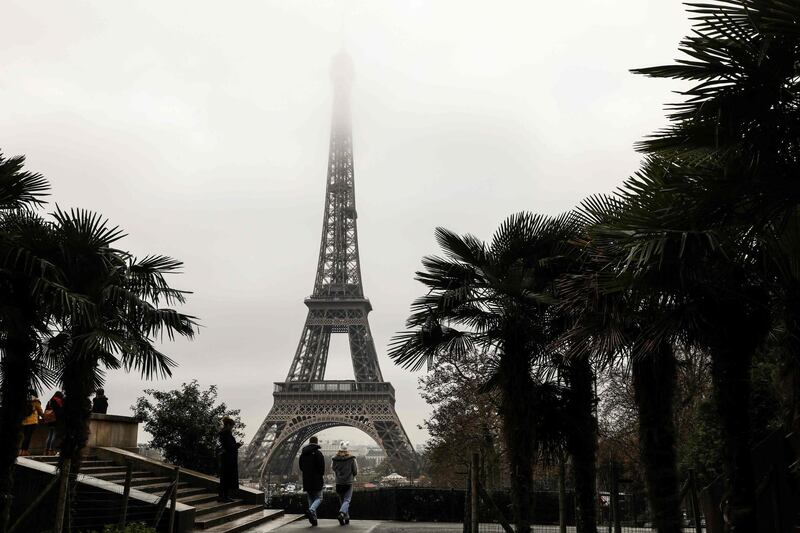 People walk at the Trocadero as France's landmark Eiffel tower is partially hidden in the fog on December 4, 2017 in Paris. / AFP PHOTO / Ludovic MARIN