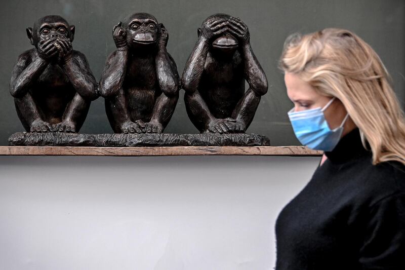 A woman wearing face mask passes a three-monkey figure on display in the pedestrian zone in Cologne, Germany. EPA