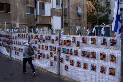 A man passes by a fence with photographs of hostages in Ramat Gan, Israel. AP Photo