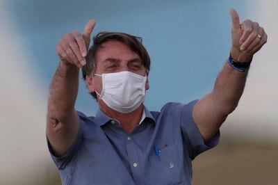 FILE - In this  July 17, 2020, file photo, Brazil's President Jair Bolsonaro who is infected with COVID-19, wears a protective face mask as he flashes thumbs-up at supporters during a Brazilian flag retreat ceremony outside his official residence Alvorada Palace, in Brasilia, Brazil. Bolsonaro announced his illness in July and used it to publicly extol hydroxychloroquine, the unproven malaria drug that heâ€™d been promoting as a treatment for COVID-19 and was taking himself. (AP Photo/Eraldo Peres, File)