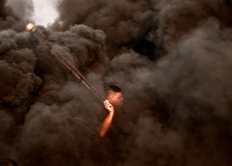 A Palestinian protester uses a slingshot in front of Israeli forces as smoke rises from burning tyres during a protest near the border with Israel, east of Gaza City. AFP
