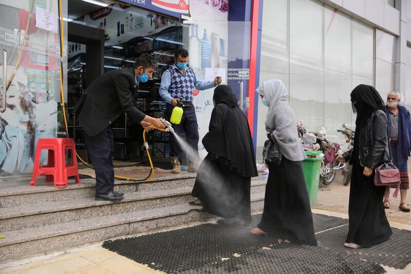 A worker disinfects the feet of women as a preventive measure against the spread of the new coronavirus before they enter a mall in Sanaa, Yemen.  AP