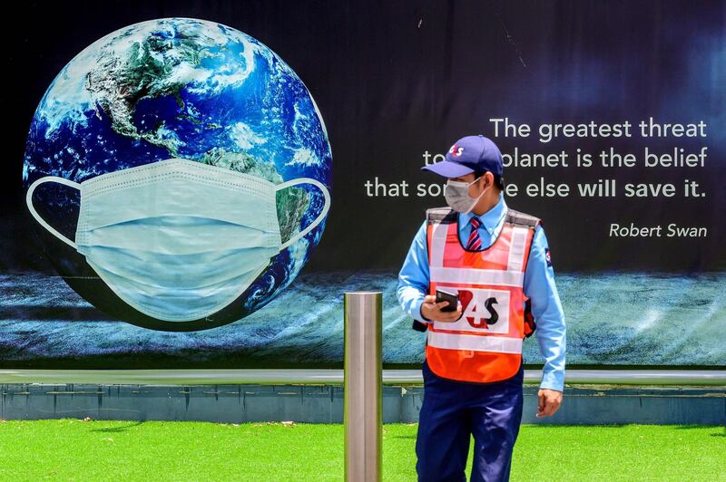 A security guard walks in front of a poster showing earth wearing a protective facemask in Bangkok on April 22, 2021, as most events marking Earth Day have been postponed due to the resurgence of the Covid-19 coronavirus in Thailand. / AFP / Mladen ANTONOV
