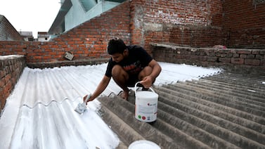 A person paints his rooftop with cool white reflective paint which brings down indoor temperatures in the summer, in Ahmedabad, India. AP