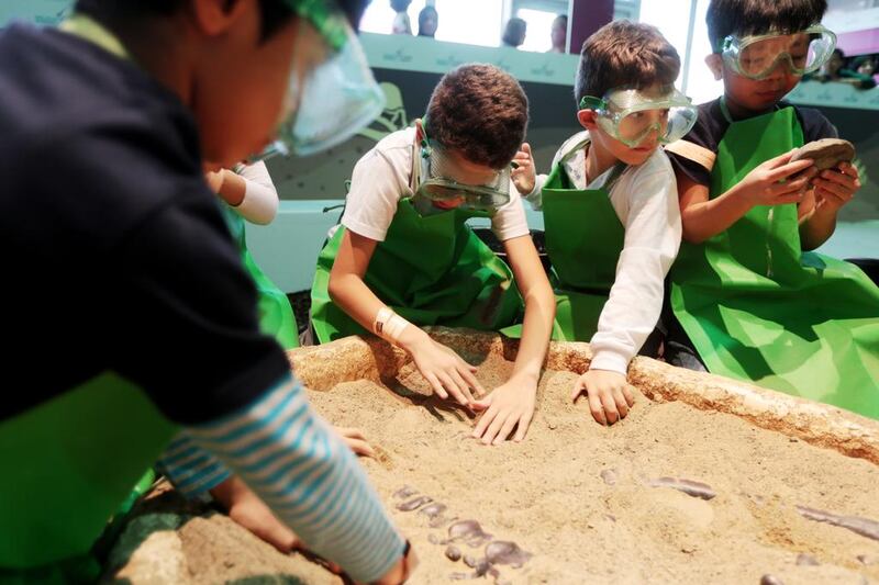 Children take part in the 'dig up a dinosaur' activity in the archaeology section of the Abu Dhabi Science Festival at Mushrif Central Park in Abu Dhabi. Christopher Pike / The National