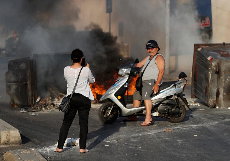 A woman, left, takes photos with her phone of her relative on his scooter in front of burned tires and garbage containers set on fire by anti-government protesters to block roads, during a protest against the economic crisis, in Beirut, Lebanon. AP Photo