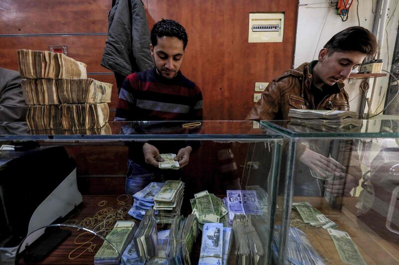 Employees of a currency exchange counter count banknotes at  market street in the northeastern Syrian town of Qamishli on May 2, 2018.  Many Kurds in Syria may dream of self-rule, but for business owners in the semi-autonomous region in the country's north, it now comes with a painful pinch: double taxes paid both to Kurdish authorities and the central government in Damascus.  / AFP / Delil souleiman
