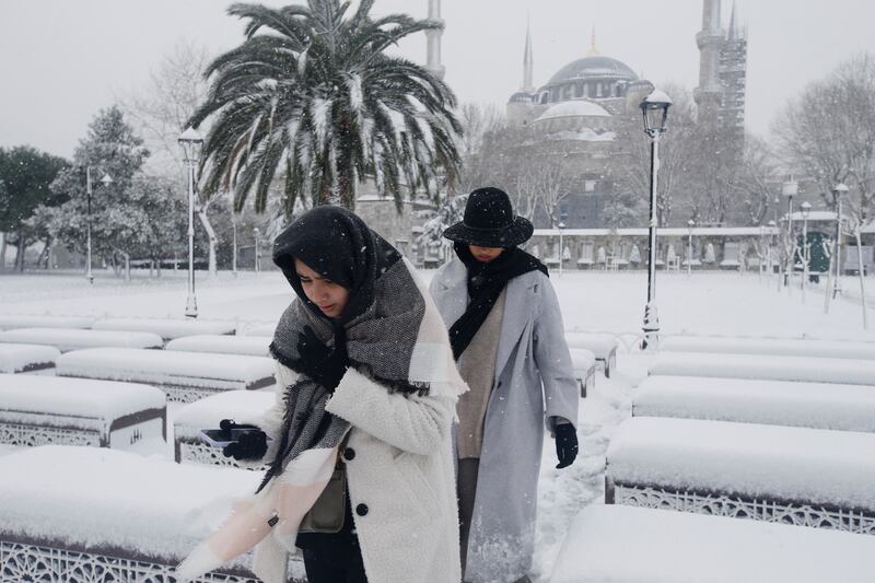 People rush for shelter from the snow, with the Blue Mosque in the background.