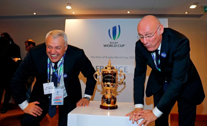President of the French bid Claude Atcher (L) and French rugby President Bernard Laporte react as they attempt to stand up after crouching for a photograph by the trophy after France was named to host the 2023 Rugby World Cup in London on November 15, 2017.
France won the right to stage the 2023 World Cup, it was announced Wednesday, despite finishing behind rival bidders South Africa in an evaluation report. / AFP PHOTO / ADRIAN DENNIS