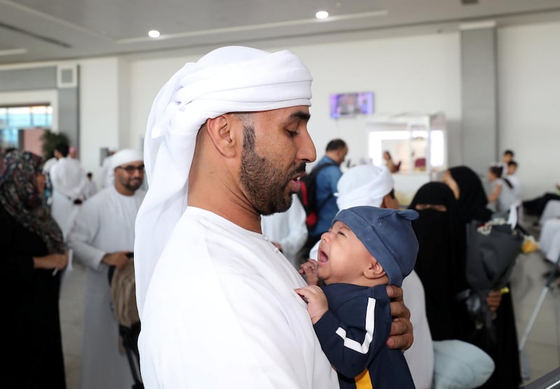 Abu Dhabi, United Arab Emirates - August 15, 2019: Malalla Alhammadi holds his son Nahayan as he returns from the Hajj pilgrimage. The pilgrims will be returning following the Eid Al Adha holiday. Thursday the 15th of August 2019. Abu Dhabi International Airport, Abu Dhabi. Chris Whiteoak / The National