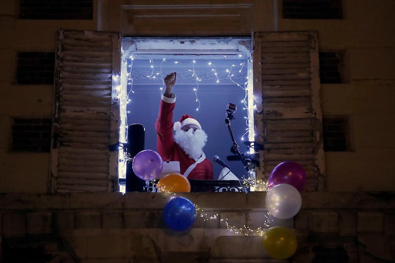 French tenor singer Stephane Senechal, dressed as Santa, sings Christmas carols at dusk from his apartment window decorated with balloons during the partial lockdown, in Paris, December 15. AP