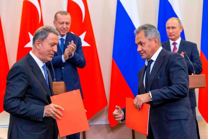 Russian Defense Minister Sergei Shoigu (frontR) exchanges documents with Turkish Defense Minister Hulusi Akar (frontL) as Russian President Vladimir Putin (backR) and Turkish President Recep Tayyip Erdogan applaud during a joint press conference following the talks, in the Bocharov Ruchei residence in the Black Sea resort of Sochi in Sochi on September 17, 2018.  The leaders of the two countries that are on opposite sides of the conflict but key global allies will discuss the situation in Idlib at Putin's residence in the Black Sea resort city of Sochi. / AFP / SPUTNIK / Alexander Zemlianichenko
