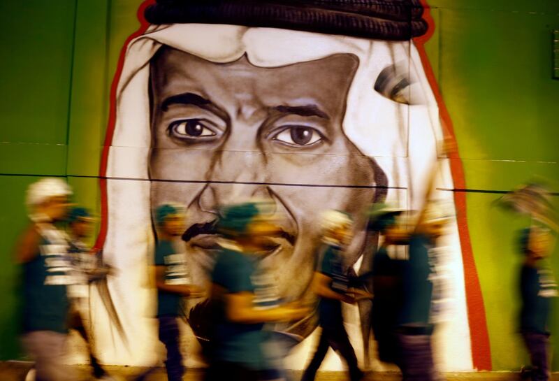 In this picture taken with low shutter speed, people walk in front of graffiti showing Saudi King Salman, marking National Day to commemorate the unification of the country as the Kingdom of Saudi Arabia, in Riyadh, Saudi Arabia, Monday, Sept. 23, 2019. (AP Photo/Amr Nabil)