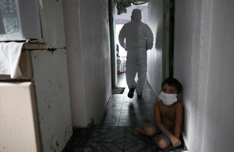 A kid looks on as a municipal healthcare worker walks after examining the body of Shirlene Morais Costa, who died at home at the age of 53 after reporting symptoms consistent with Covid-19, in Manaus, Brazil. Reuters