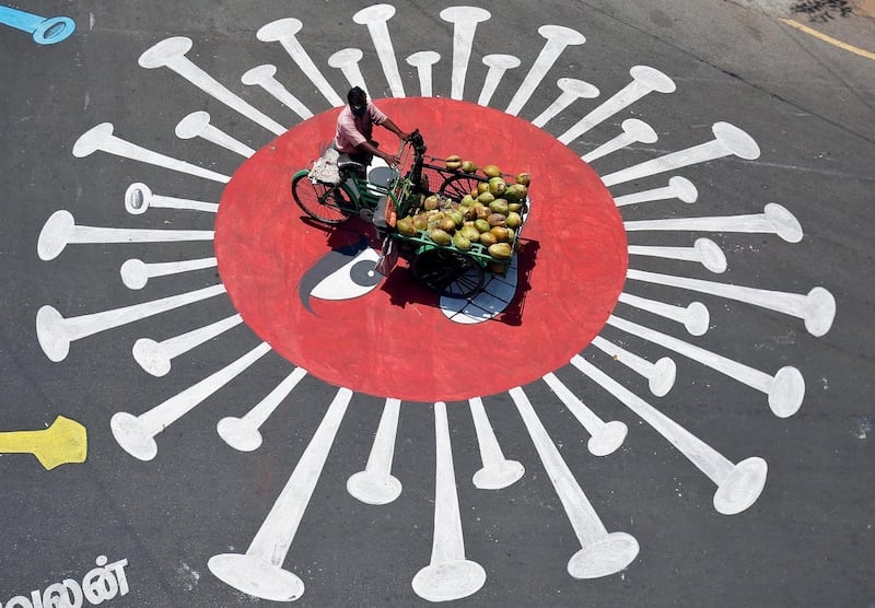 A man selling coconuts rides his trishaw across graffiti depicting the coronavirus in Chennai, India. Reuters