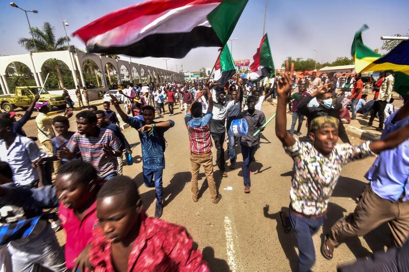 Sudanese demonstrators march with national flags as they gather during a rally demanding a civilian body to lead the transition to democracy, outside the army headquarters in the Sudanese capital Khartoum on April 13, 2019. - Sudan's new military leader General Awad Ibn Ouf resigned late on April 12 just a day after being sworn in, as the country's army rulers insisted they would pave the way for a civilian government. (Photo by AHMED MUSTAFA / AFP)